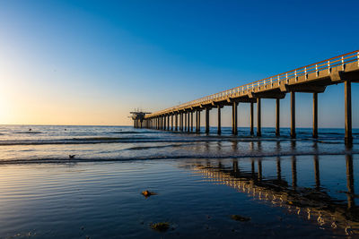 Pier over sea against clear sky during sunset