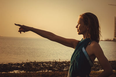 Woman pointing while standing by sea against sky during sunset