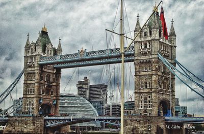 Low angle view of suspension bridge in city against cloudy sky