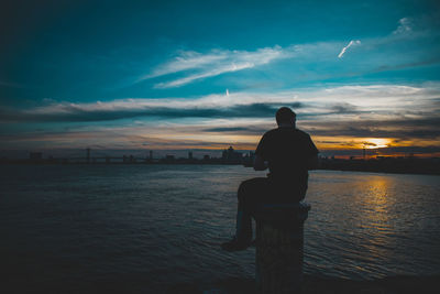 Silhouette man looking at sea against sky during sunset