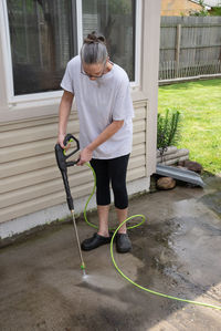 Woman pressure washes the algae growth from the patio and sidewalk