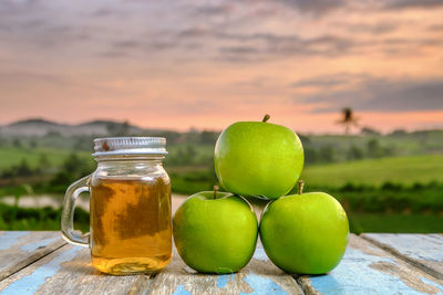 Granny smith apples by honey jar on table against sky during sunset