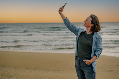 A young woman on the beach near the ocean in the spring at sunset takes a selfie, talks via video