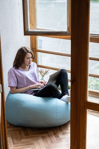 Young woman using laptop on sunny balcony. working at home, freelance concept.