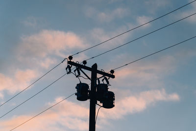 Low angle view of silhouette powerlines and telephone pole  against sunset sky.