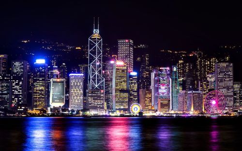 Illuminated victoria harbour - hong kong by river against sky at night