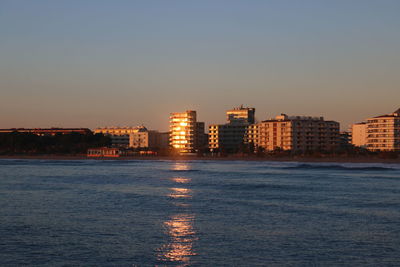 Sea and buildings against sky during sunset