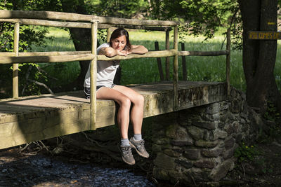 Fit woman sitting and relaxing on a wooden bridge in the middle