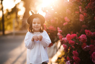 Smiling baby girl 3-4 year old wearstylish clothes and having fun over roses at background outdoor