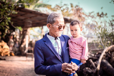 Grandfather carrying granddaughter while standing outdoors