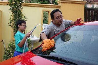 Boy assisting father while washing car