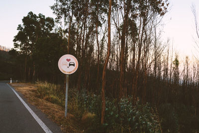 Road sign by trees against sky