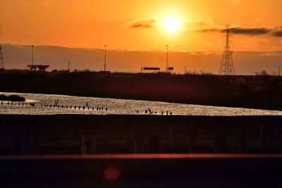 Silhouette electricity pylon against orange sky during sunset