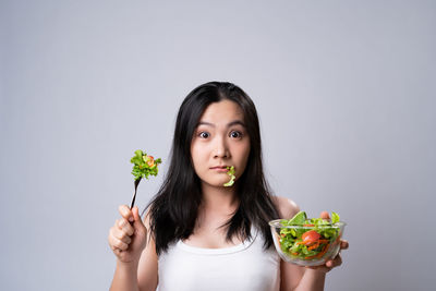 Portrait of woman holding ice cream against white background