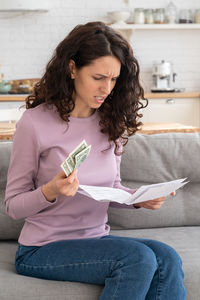 Angry woman holding bill while sitting at home