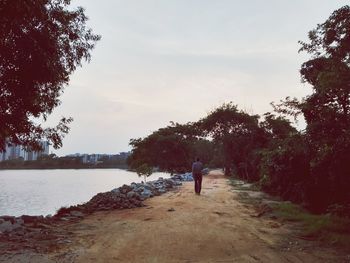 Rear view of woman walking on lake against sky