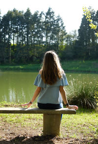 Rear view of teenage girl standing on bench by lake