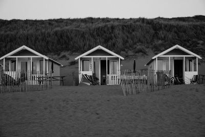 Hut on beach by houses against sky