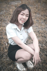 Portrait of young woman crouching on field