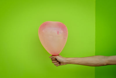 Cropped image of hand holding balloons against green background