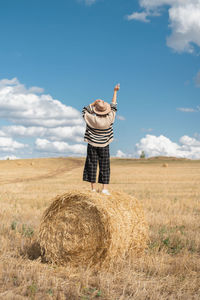 Man standing by hay bales on field against sky