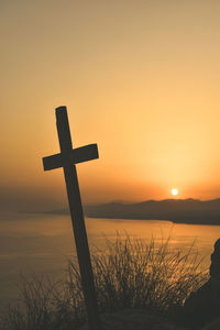 Silhouette cross on shore against sky during sunset