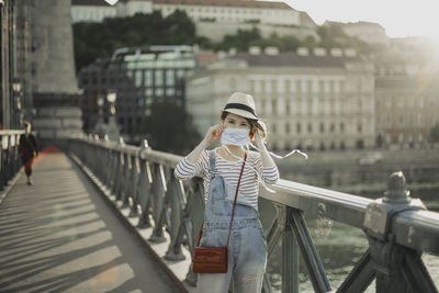 Portrait of young woman wearing face mask on bridge in city