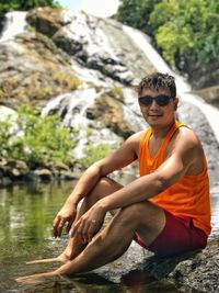 Portrait of man sitting on rock by river