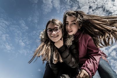 Low angle portrait of sisters bending against blue sky