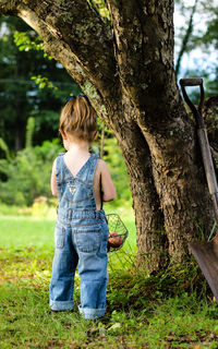 Full length rear view of girl standing by tree trunk at park