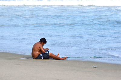 Shirtless boy sitting at sea shore