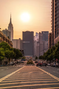 City street by buildings against sky during sunset