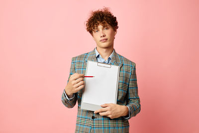 Portrait of young man showing clipboard against pink background