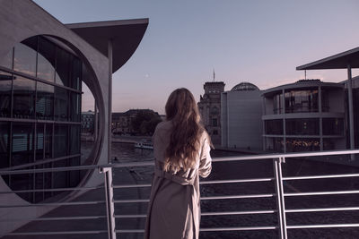 Rear view of woman leaning on railing against sky