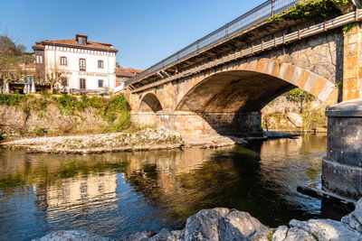 Bridge over river by old building against sky