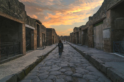 Rear view of woman walking on footpath against sky during sunset