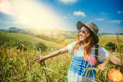 Smiling woman wearing hat standing on field against sky