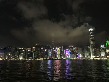 Illuminated buildings by river against sky at night