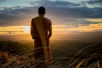 Rear view of man standing on field against sky at sunset