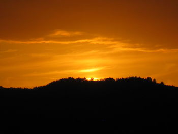 Silhouette trees against dramatic sky during sunset