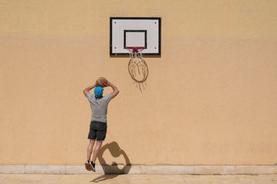 Rear view of man playing basketball against wall