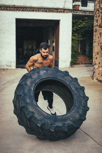 Male athlete pushing tire during sports training on street