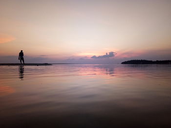 Silhouette person standing on pier over lake against sky during sunset