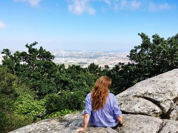 Rear view of woman sitting on rock against sky