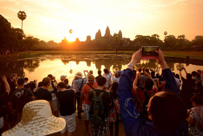 People photographing against lake and sky during sunset