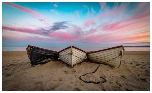 Deck chairs on beach against sky during sunset