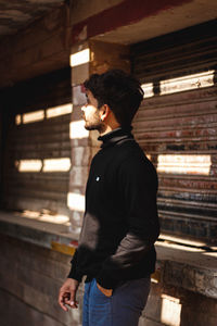 Side view of young man standing against building