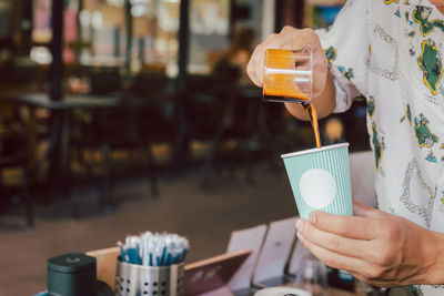 Barista pours iblack coffee into a takeaway paper cup.