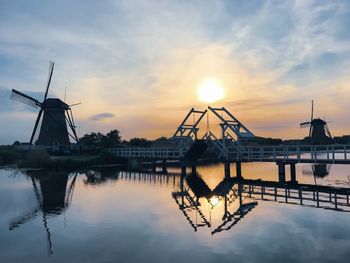 Cranes at riverbank against sky during sunset