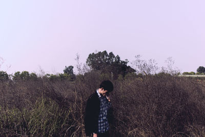 Young man smoking cigarette on field against clear sky